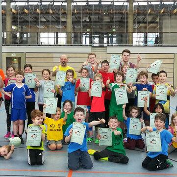 Gruppenfoto von 30 Kindern in Sportkleidung, die stolz ihre Urkunden in einer Turnhalle pr&auml;sentieren.