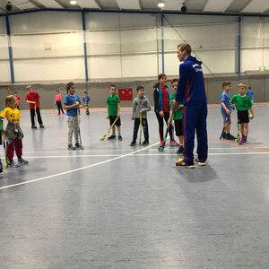 Gruppentraining f&uuml;r Kinder in einer Sporthalle, ein Trainer erkl&auml;rt &Uuml;bungen, verschiedene farbige Trikots.