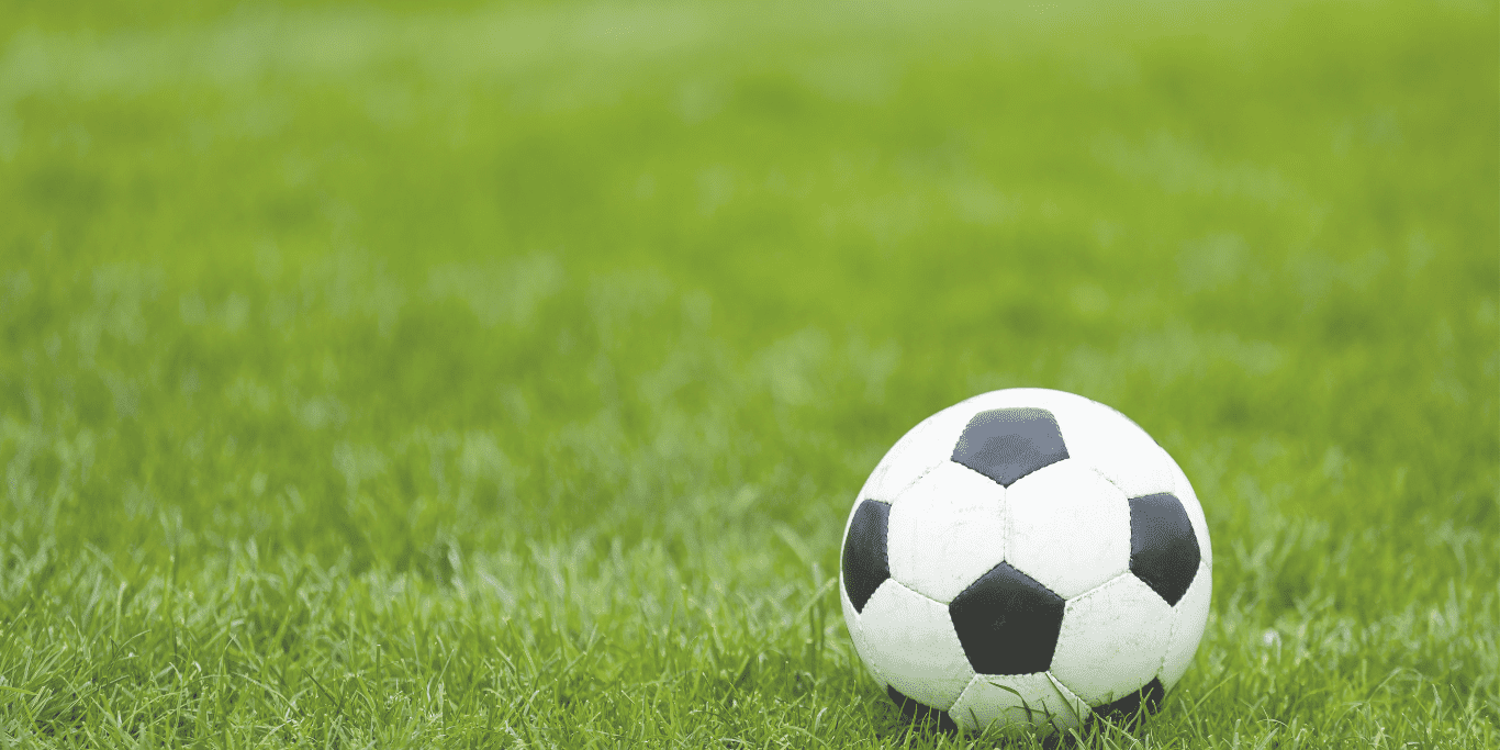 Ein Fußball liegt auf grünem Rasen, gut sichtbar im Vordergrund der Aufnahme.