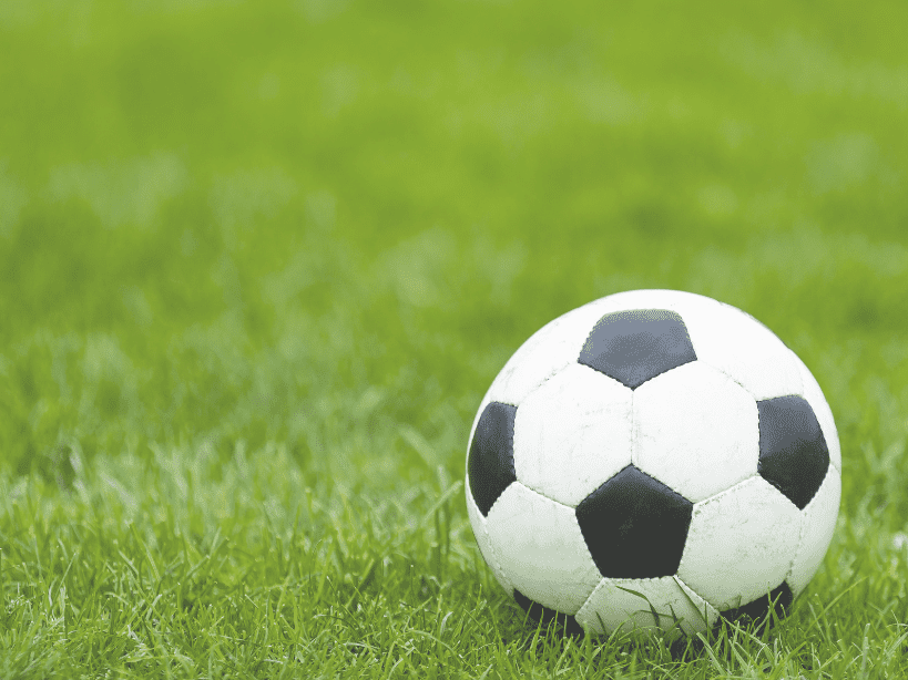 Ein Fu&szlig;ball liegt auf gr&uuml;nem Rasen, gut sichtbar im Vordergrund der Aufnahme.