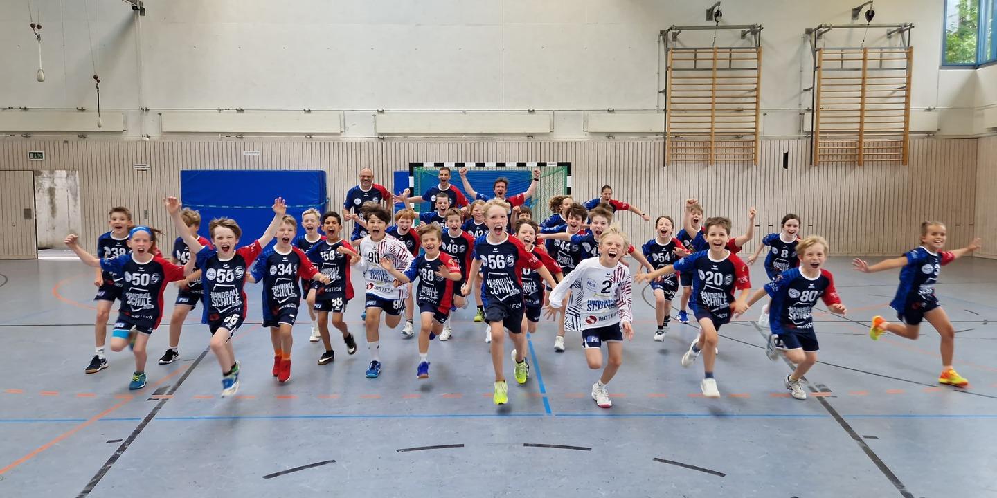 Gruppe von Kindern in Sportkleidung l&auml;uft begeistert in einer Halle, einige jubeln, andere lachen.