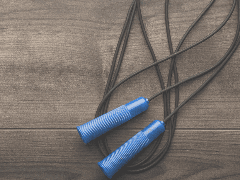 Springseil mit blauen Griffen auf einer Holzoberfl&auml;che, in einer lockeren Schlaufe liegend.