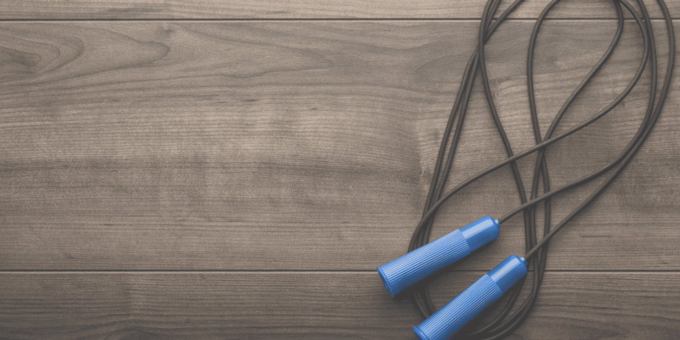 Springseil mit blauen Griffen auf einer Holzoberfl&auml;che, in einer lockeren Schlaufe liegend.