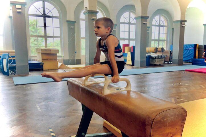 Junge f&uuml;hrt eine &Uuml;bung an einem Barren in einem Turnraum mit gro&szlig;en Fenstern aus.
