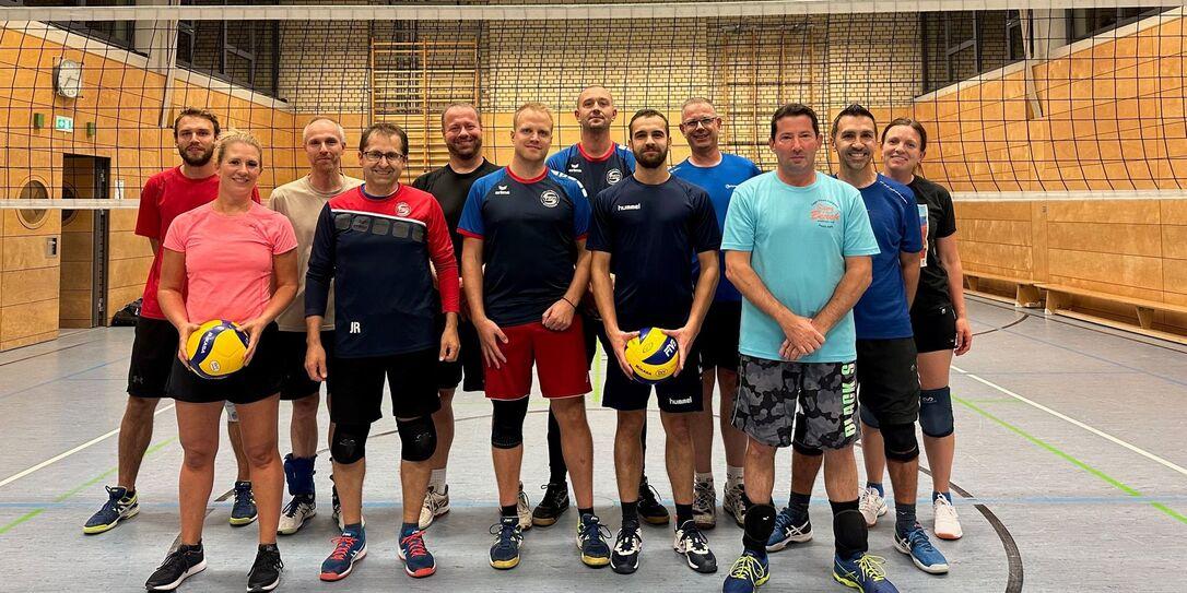Gruppenfoto von 14 Volleyballspielern in Sportkleidung, gehalten vor einem Volleyballnetz in einer Sporthalle.