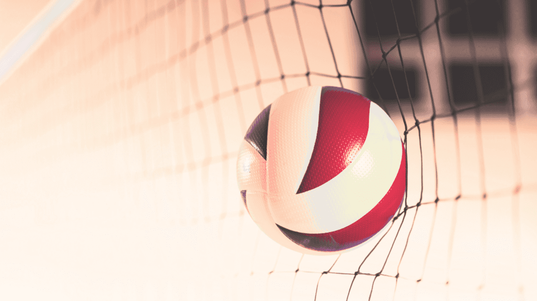 Nahaufnahme eines Volleyballs, der im Netz h&auml;ngt, mit rot-wei&szlig;er Farbgebung auf einem blassen Hintergrund.