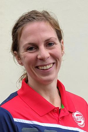 Frau mit l&auml;chelndem Gesicht tr&auml;gt ein rot-blaues Sportshirt vor neutralem Hintergrund.