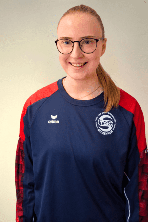 L&auml;chelnde Frau mit Brille tr&auml;gt ein dunkelblaues Trikot mit roten &Auml;rmeln und dem Logo der TSG Eckenhagen.