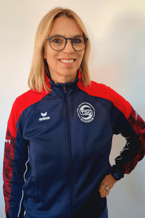 Frau mit blonden Haaren in Sportjacke der FSG Rückenwind steht vor einer weißen Wand und lächelt.