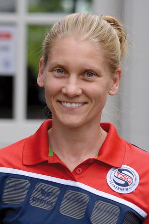 Lächelnde Frau mit blonden Haaren, trägt ein rotes Polo-Shirt mit Vereinslogo von TSG Seckenheim.