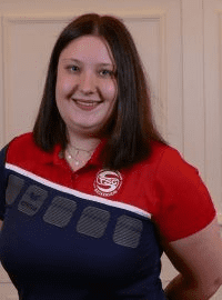 Porträt einer lächelnden Frau mit langen Haaren, bekleidet mit einem rot-blauen Poloshirt.