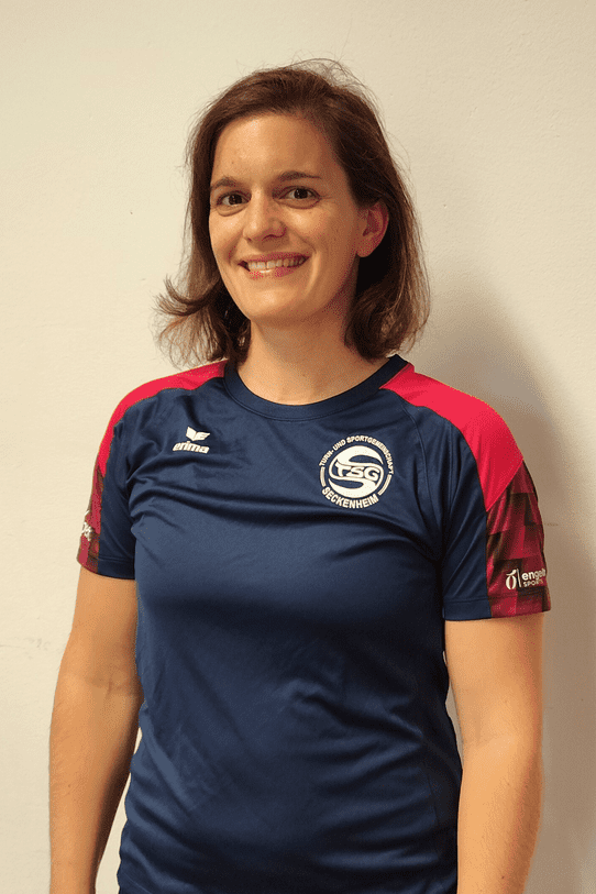 Frau mit kurz geschnittenem Haar tr&auml;gt ein blaues Sportshirt mit rot-schwarzen &Auml;rmeln und l&auml;chelt vor einer wei&szlig;en Wand.