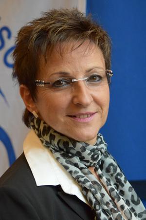 Porträt einer Frau mit kurzen, braunen Haaren, Brille und einem Leopardenmuster-Schal, vor blauem Hintergrund.