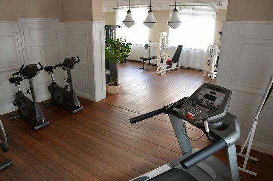Fitnessraum mit zwei Fahrradern und einem Laufband in einem hellen, mit Holzboden ausgestatteten Raum.