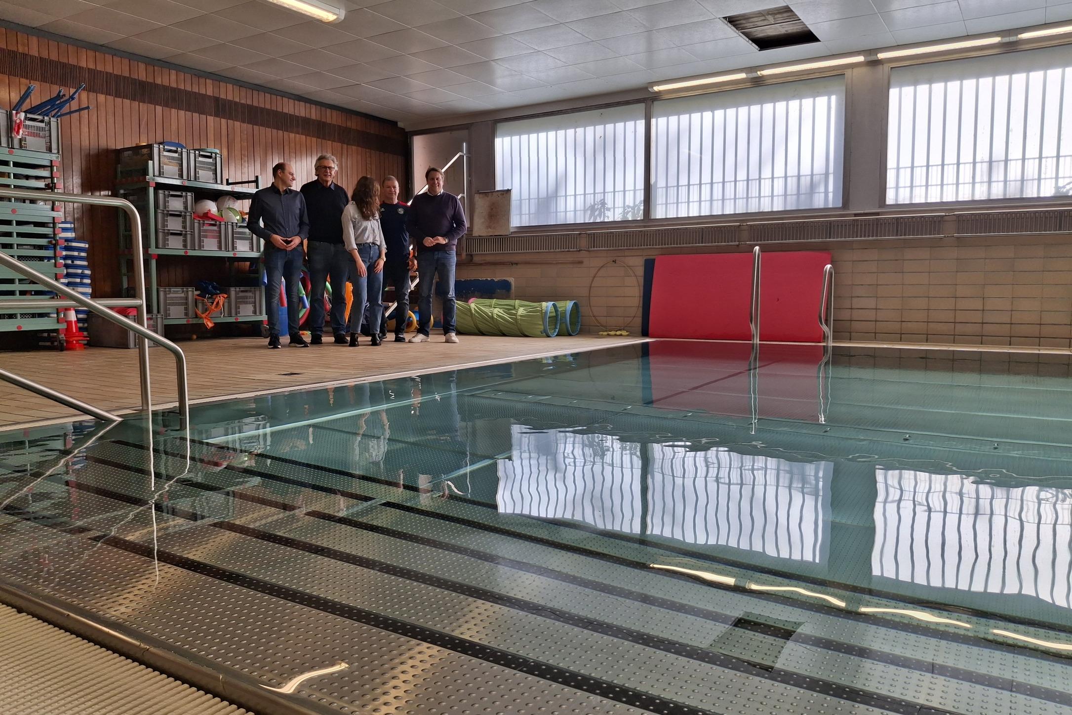 Eine Gruppe von fünf Personen steht am Beckenrand eines Schwimmbeckens in einem indoor Schwimmbad.