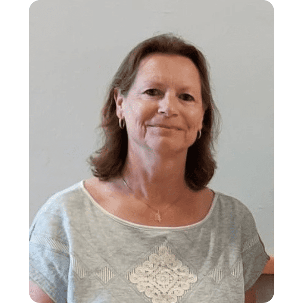 Portr&auml;t einer Frau mit mittellangen, lockigen Haaren, die ein graues T-Shirt tr&auml;gt, vor neutralem Hintergrund.