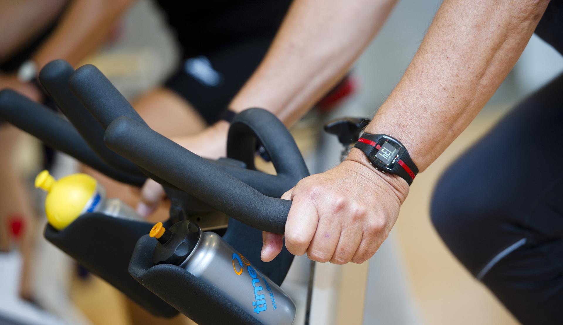 Nahaufnahme von Händen, die an den Lenkern eines Spin- und Getränkeflaschenhalter eines Fitnessbikes greifen.