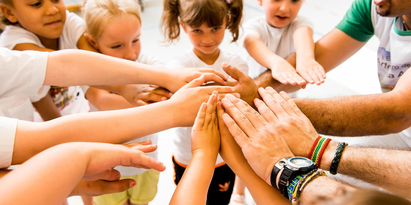Kinder und Erwachsene legen ihre Hände in einem Kreis zusammen, symbolisieren Zusammenarbeit und Gemeinschaft.
