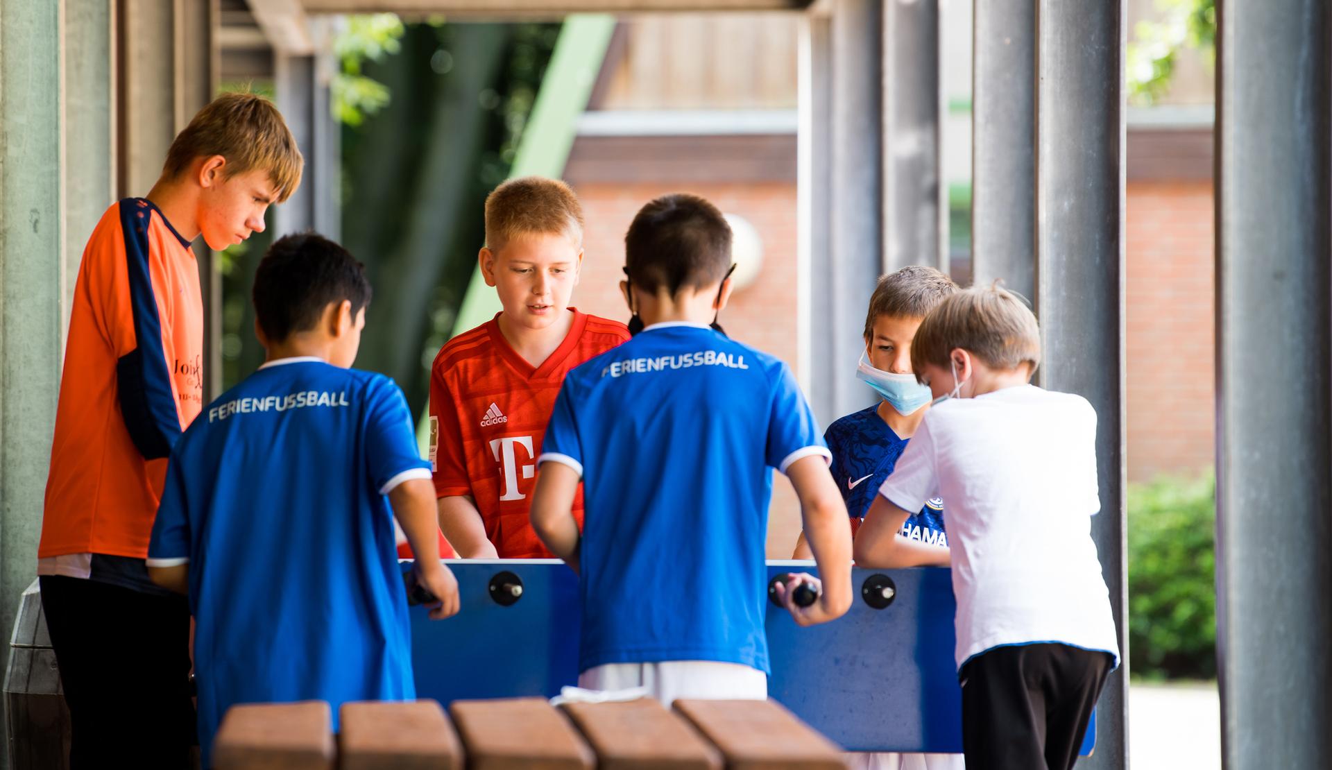 Sechs Kinder spielen gemeinsam mit einem Tischkicker unter einem überdachten Bereich.