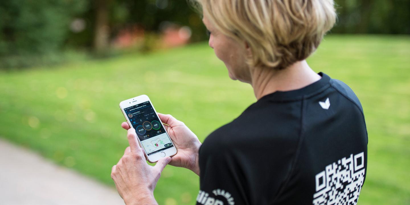 Frau mit kurzen Haaren schaut auf ein Smartphone, während sie auf einem Weg in einem Park steht.