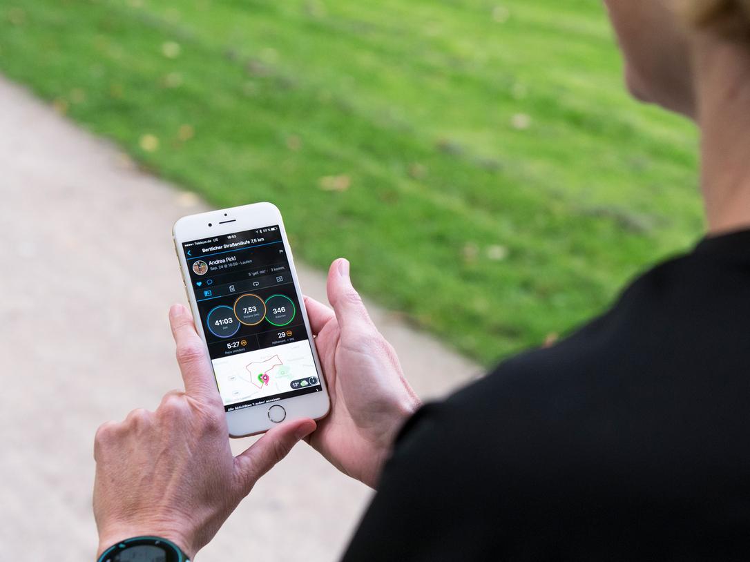 Person hält ein Smartphone mit Laufstatistiken in der Hand, während sie auf einem Weg im Freien steht.