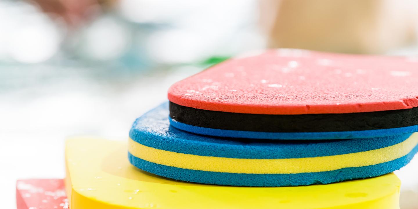 Bunte Schwimmbretter in verschiedenen Farben übereinander gestapelt, mit Wassertropfen auf der Oberfläche.